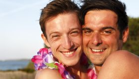 Two men embracing outdoors, one wearing lei
