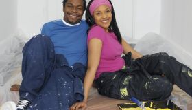 Young man and woman sitting on floor in decorating overalls, smiling