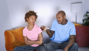 African man pointing remote control at annoyed girlfriend
