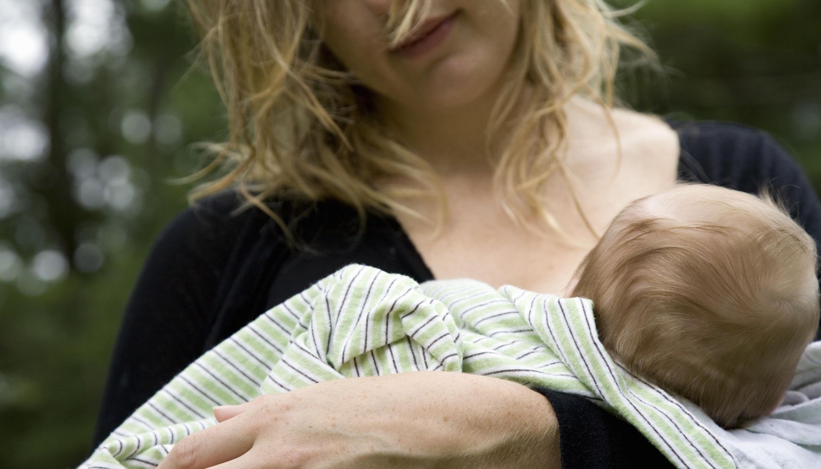 Mother breastfeeding baby girl (2-4 months) outdoors, mid section