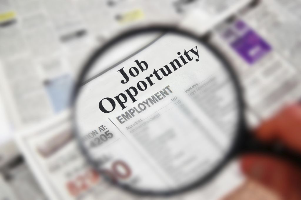 Magnifying glass over a newspaper classified section with "Job Opportunity" text