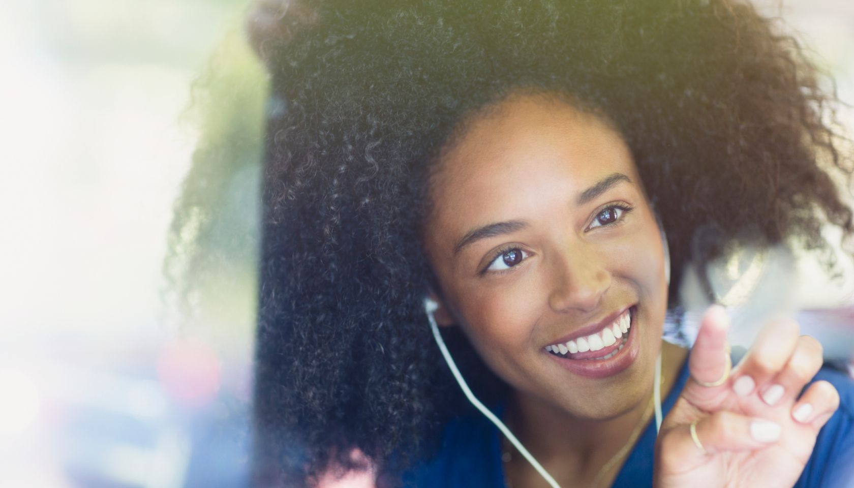 Smiling woman with afro and headphones drawing heart-shape on bus window