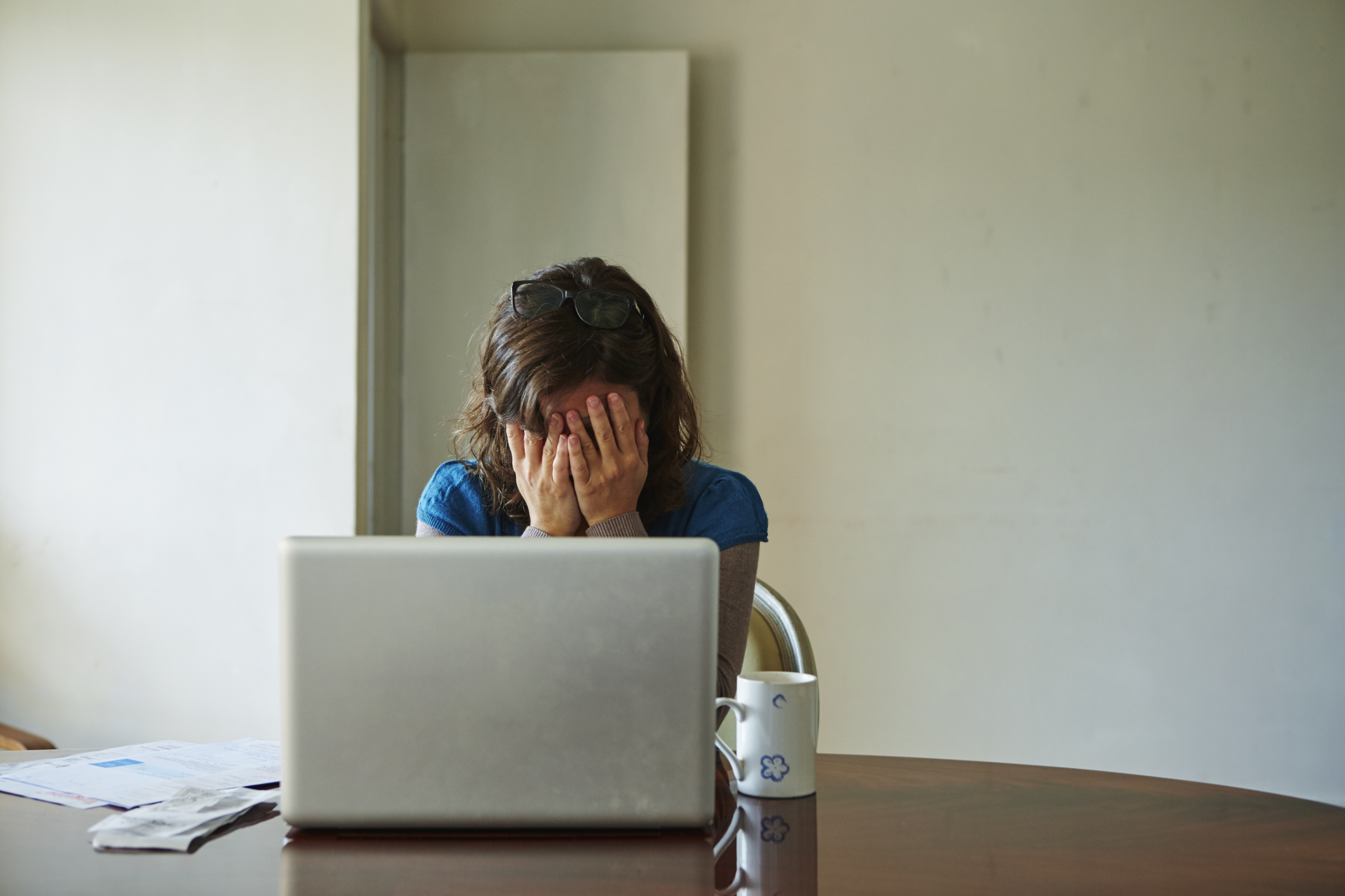 Young woman sitting at table using laptop, looking stressed