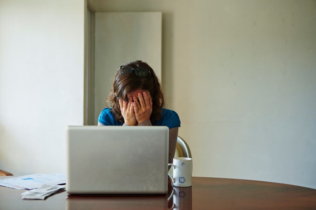 Young woman sitting at table using laptop, looking stressed
