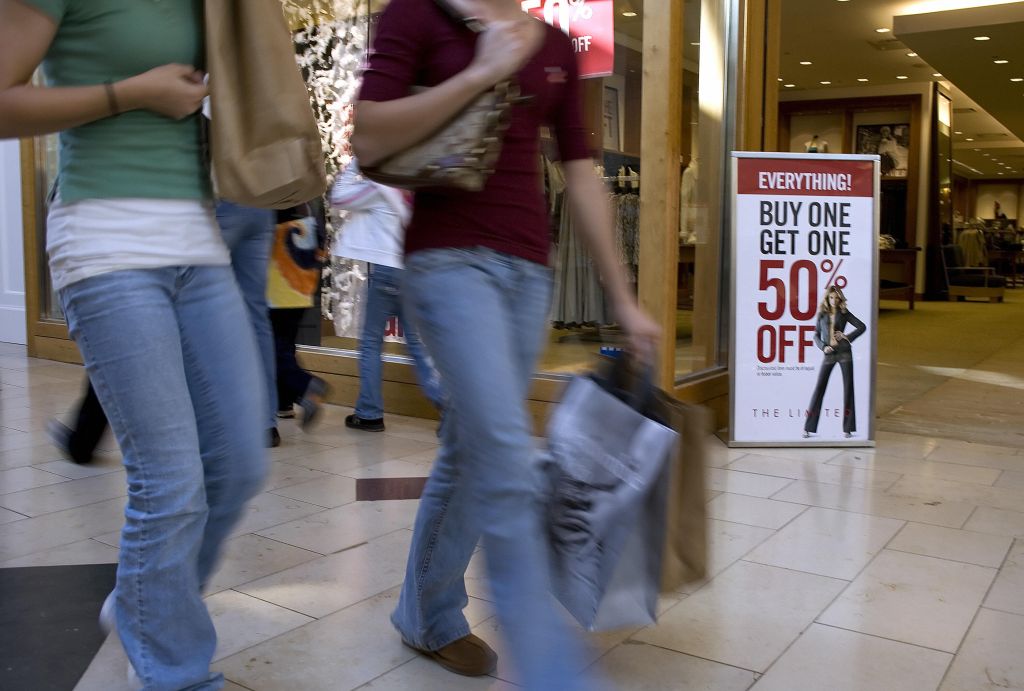 Shoppers walk past a sale sign in front