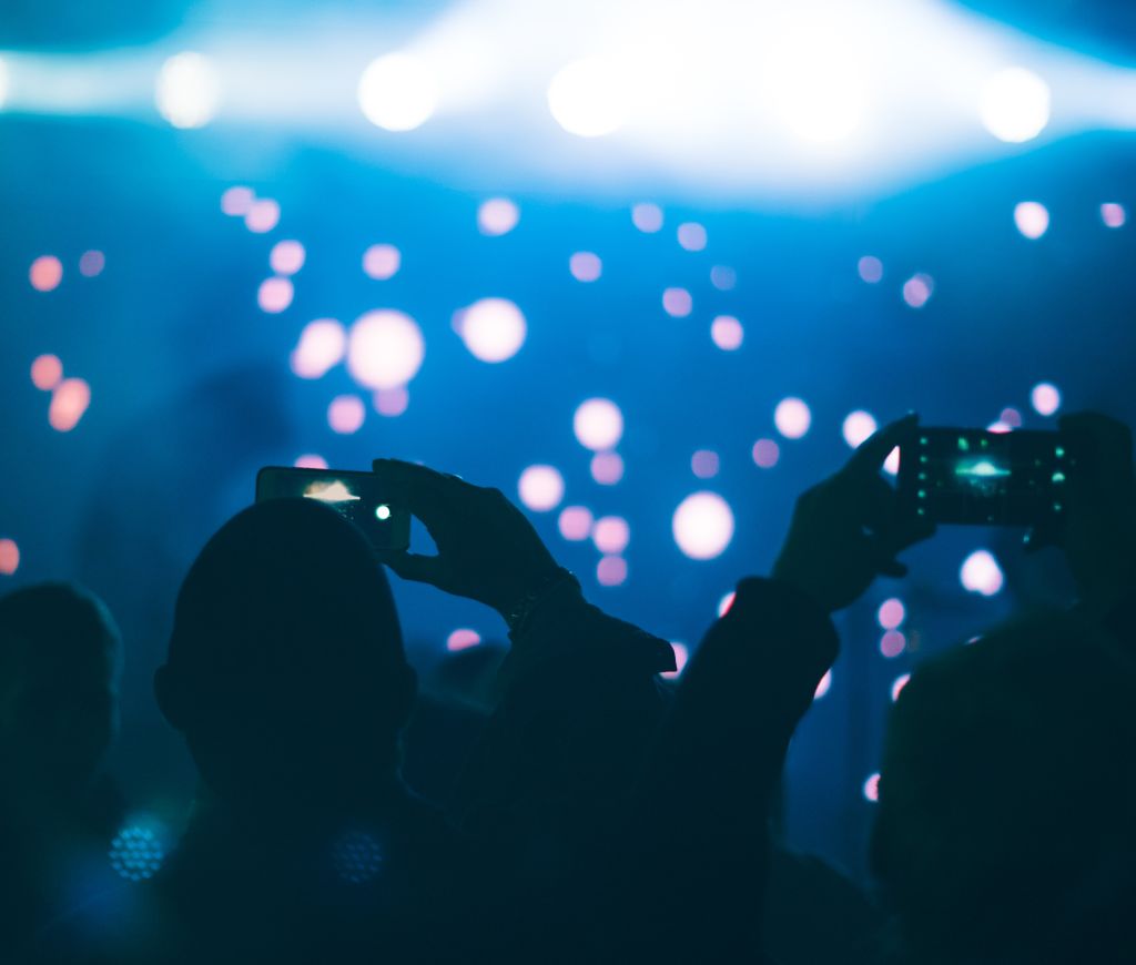 Audience members taking photos with mobile phones in a concert, against stage & spotlights