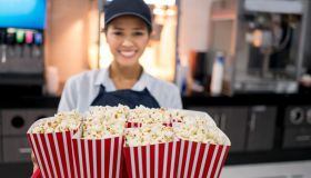 Happy woman working at the movie theatre selling popcorn