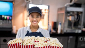 Happy woman working at the movie theatre selling popcorn