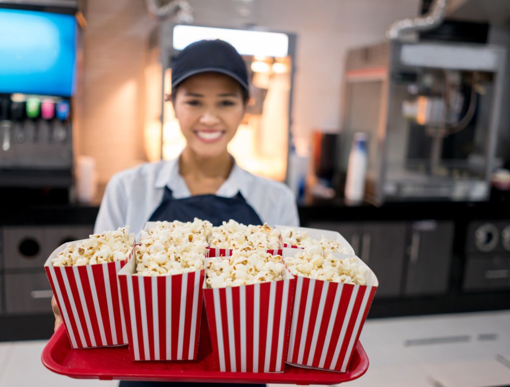 Happy woman working at the movie theatre selling popcorn