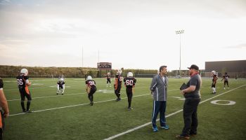 Coaches talking near teenage boy high school football team on football field