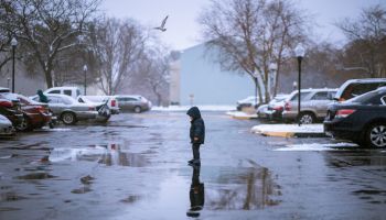 Side View Of Boy Standing On Wet Footpath During Winter