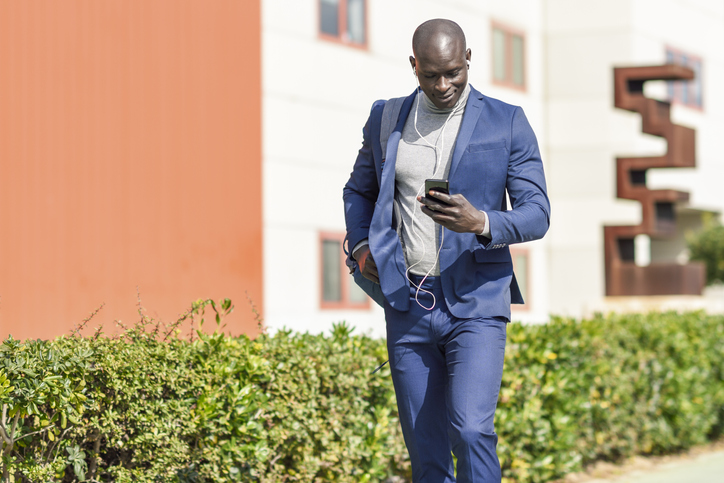 Businessman wearing blue suit listening music with earphones and smartphone