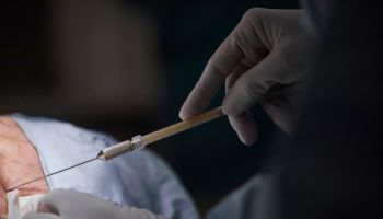Hands of female surgeon injecting patient in dark