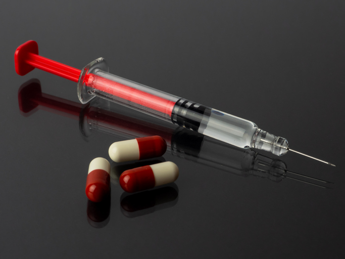 A syringe and several pills reflected on a gray background with mirror effect