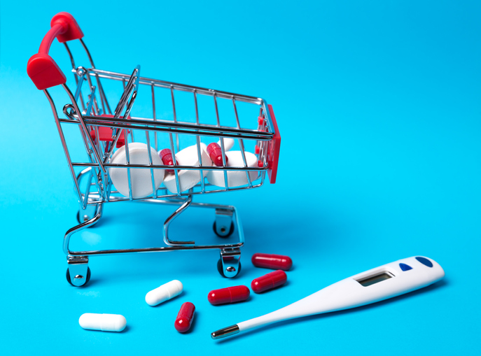 Pills and thermometer, tablets in the toy trolley for shopping on blue background. The concept of treating cold diseases.