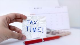Tax time concept; hand is holding Tax Time written on the white paper note with a red pen and calendar.