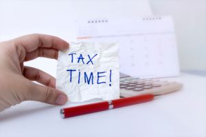 Tax time concept; hand is holding Tax Time written on the white paper note with a red pen and calendar.