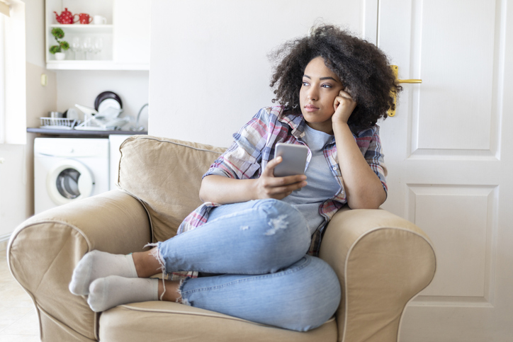 Pensive young woman using smart phone at home