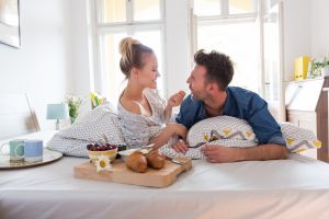 Happy couple eating breakfast in the bed at home