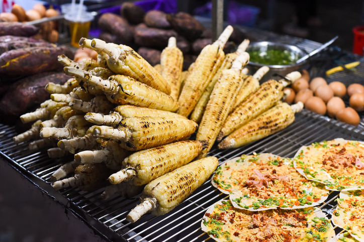 Grilled corn near vietnamese pancake with eggs, sausages and sauces in vietnamese night market in Da Lat