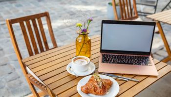A laptop, croissant, and coffee on a cafe's summer terrace