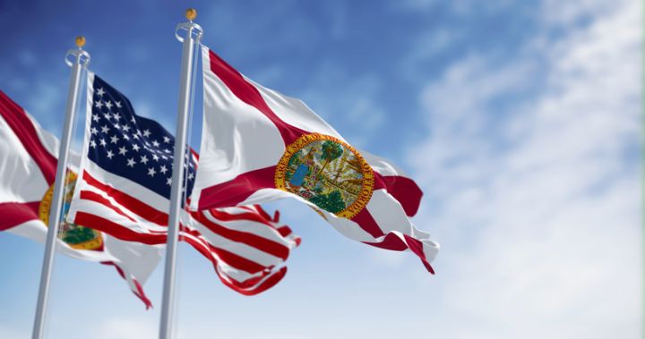 The flags of Florida and United States waving in the wind on a clear day