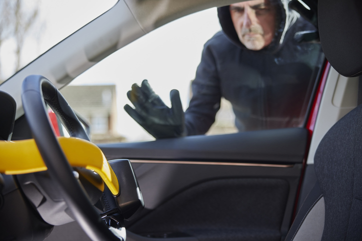 Male Thief Looking Through Window At Manual Steering Wheel Lock In Car