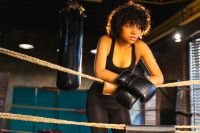 Woman fighter girl power. African american woman fighter with boxing gloves standing on boxing ring leaning on ropes waiting and resting. Strong powerful girl. Strength fit body workout training.