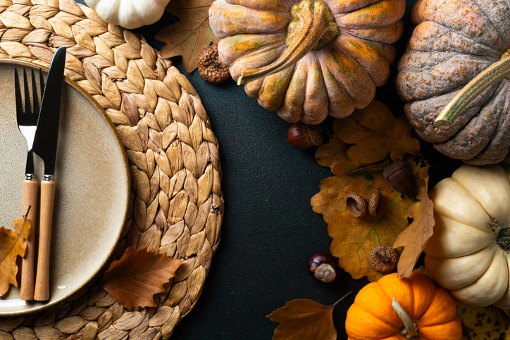 Cozy hygge table. Top view of plate and cutlery, pumpkins, autumn leaves on dark table. Autumn table setting. Festive Thanksgiving or Halloween background. Restaurant menu