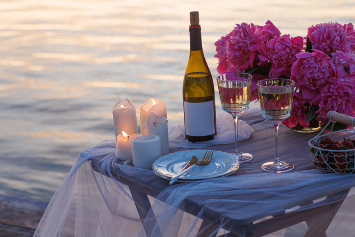 Romantic sunset dinner on the beach. Table honeymoon set for two with luxurious food, glasses of champagne drinks in a restaurant with sea view. Summer love, romance date on vacation concept.