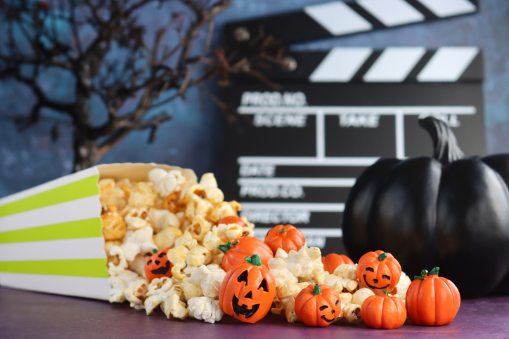 Image of halloween movie night with jack-o’-lanterns under autumn tree / popcorn, pumpkins, clapperboard, haunted house decorations