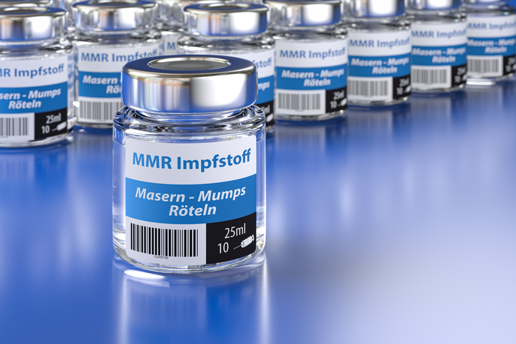 Vials of a fictitious MMR (Measles, Mumps, Rubella) vaccine with German language label (Masern, Mumps, Röteln). Large group of vials with one standing in front, selective focus on foreground