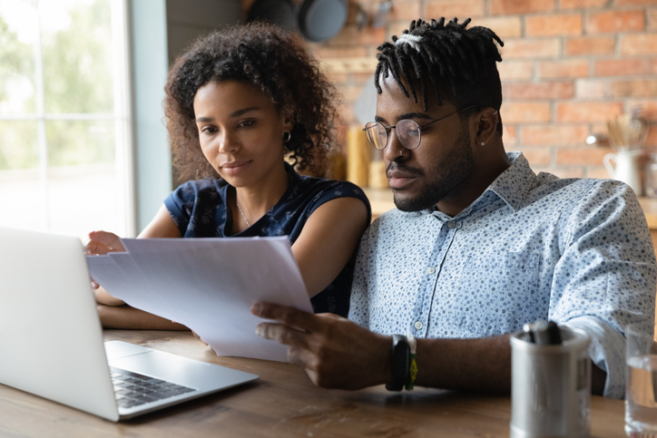 Serious millennial black married couple reading documents at laptop together