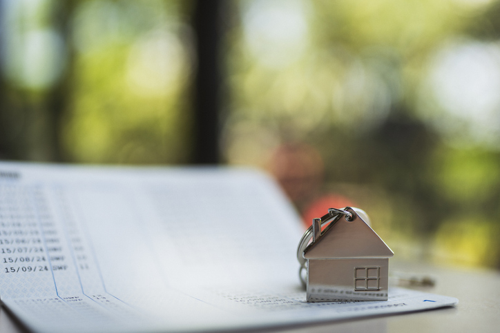 House model key with bank account book on wooden table, representing home loan, mortgage planning, real estate investment, and financial saving for future property ownership in natural light.