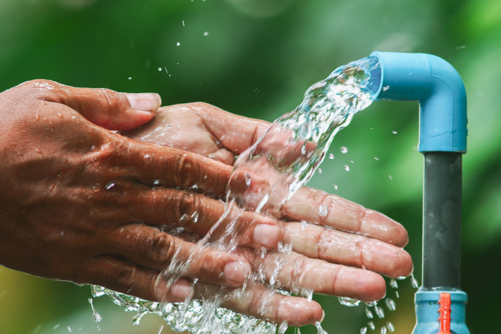 Hands being washed under a flowing tap, emphasizing hygiene and cleanliness with a natural green backdrop.