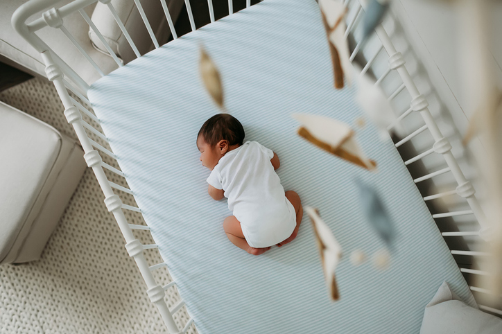 Overhead look at a newborn baby in his crib with a mobile in view