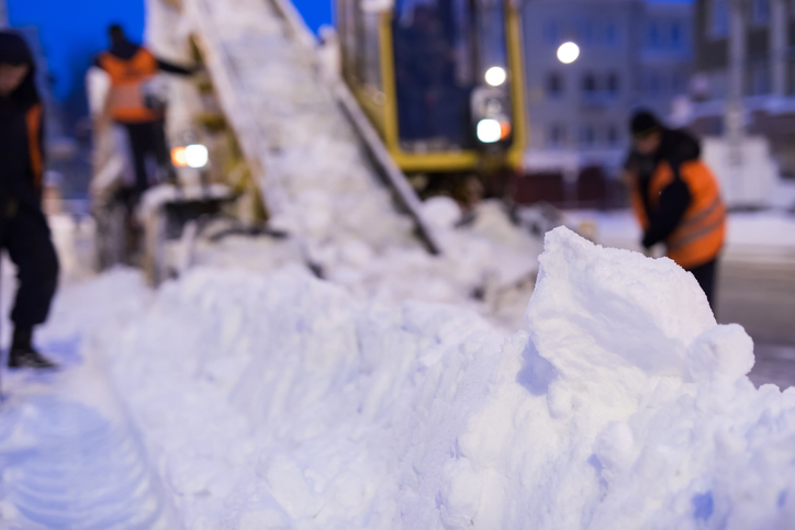 Claw loader vehicle removes snow from the road. Uniformed worker helps shovel snow into a snowplow.