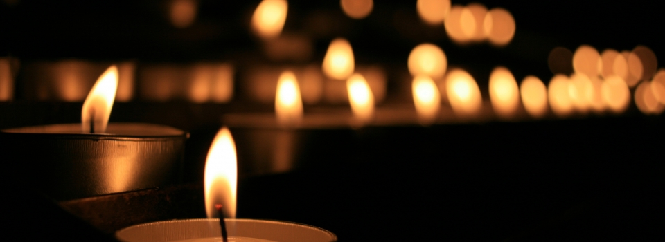 Rows of lit candles in a dark setting, creating a warm, serene atmosphere.
