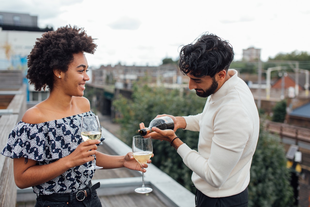 A young couple enjoying drinks on a balcony, with the city skyline in the background.