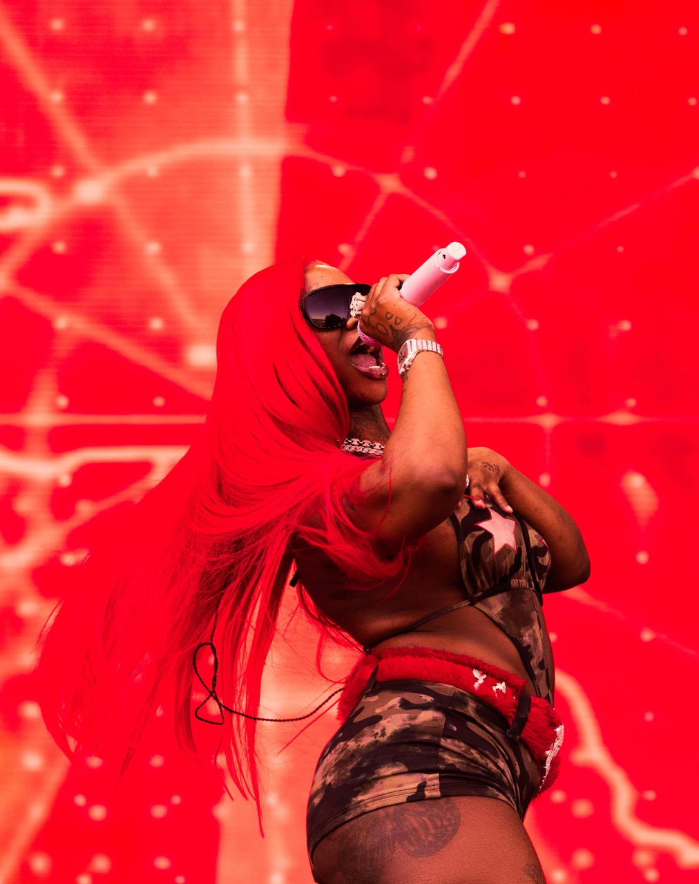 A person wearing a red hooded outfit and sunglasses performing on a brightly lit stage.