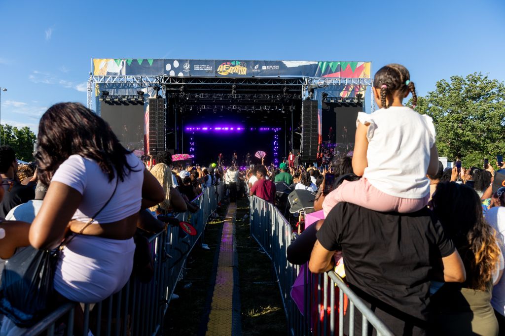 A large outdoor music festival stage with a colorful, patterned backdrop and a crowd of people in the foreground watching the performance.