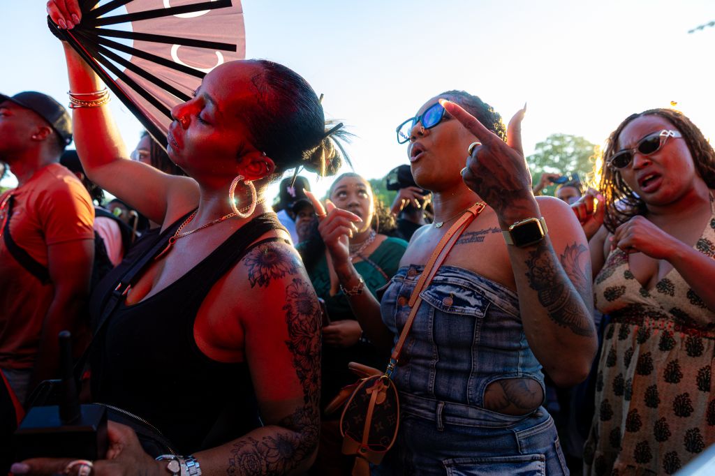 A crowd of people at an outdoor festival, some wearing colorful clothing and accessories, dancing and celebrating.