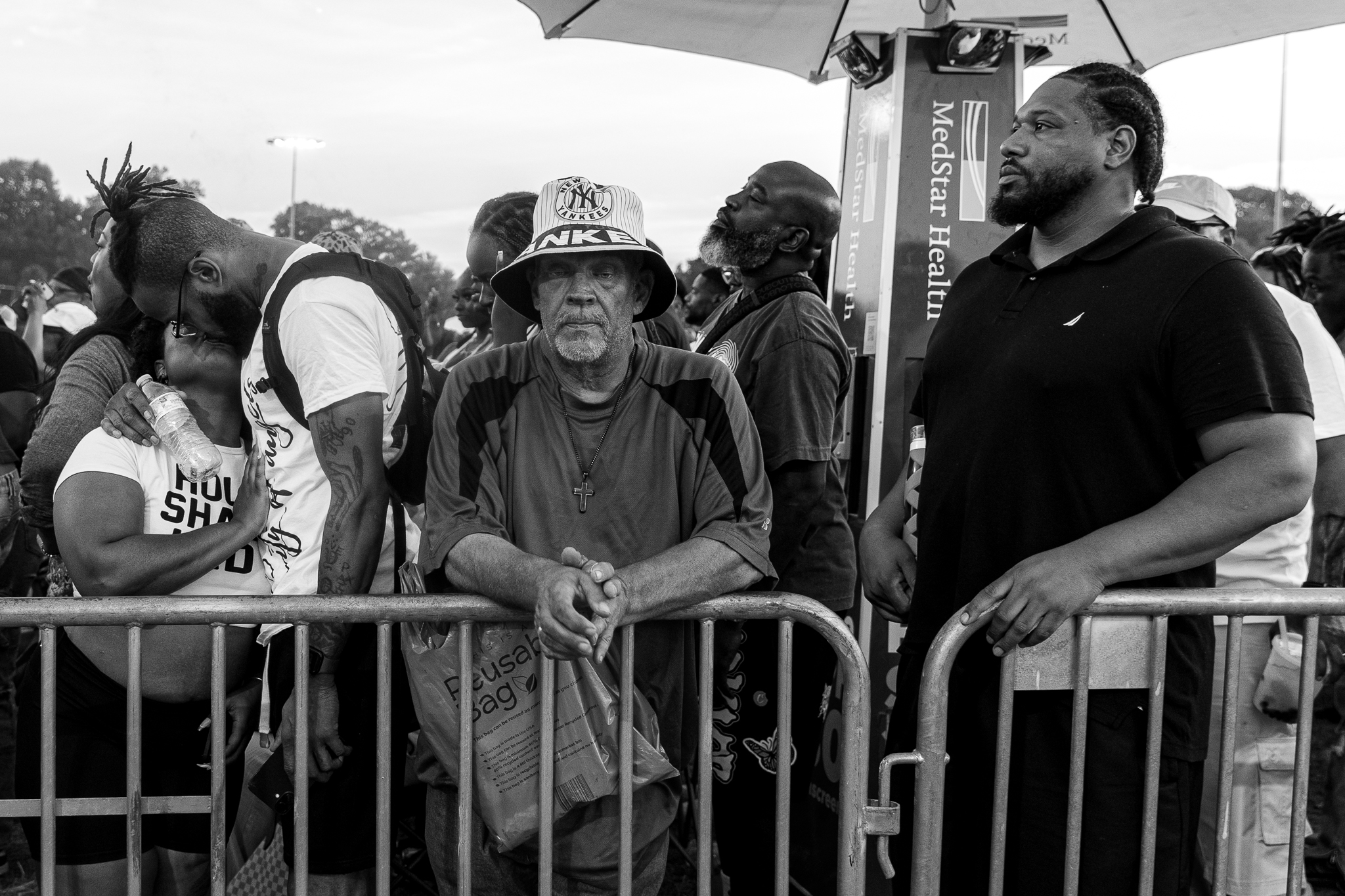 A group of people gathered at a protest, including a man wearing a Nike hat and holding a sign, and another man wearing a black shirt.