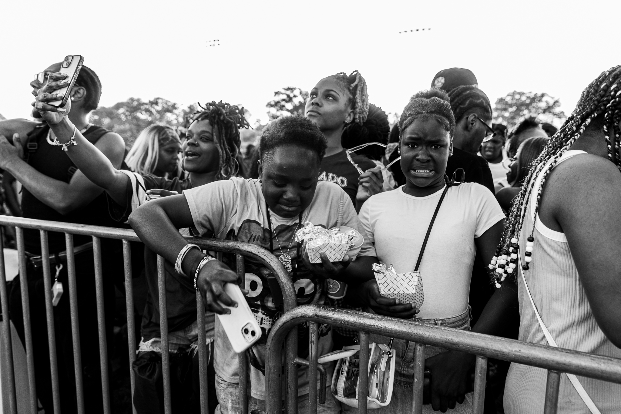 A crowd of people, mostly young Black individuals, gathered at a festival or event. Some are holding up their phones to take photos or videos.