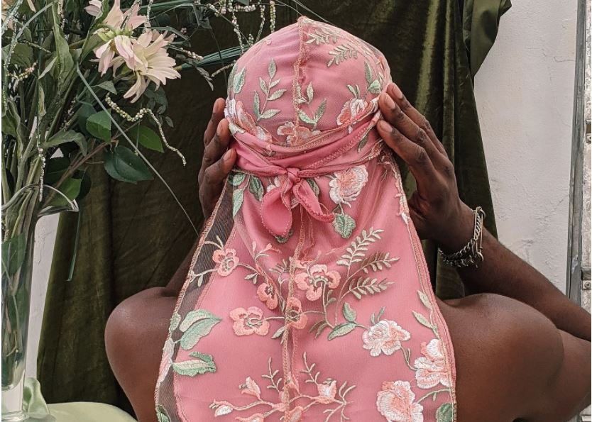 Hands holding a pink floral-patterned headscarf against a lush, green background.