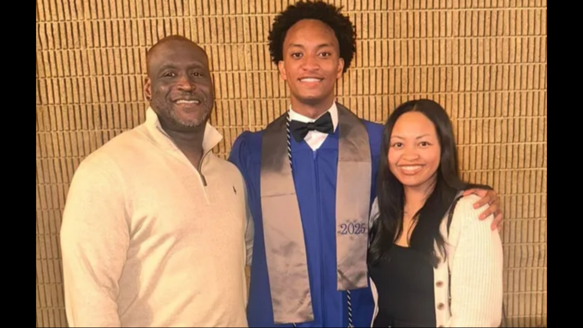 Three people posing for a photo - a smiling man in a beige sweater, a young man in a blue graduation gown, and a smiling woman in a black sweater.