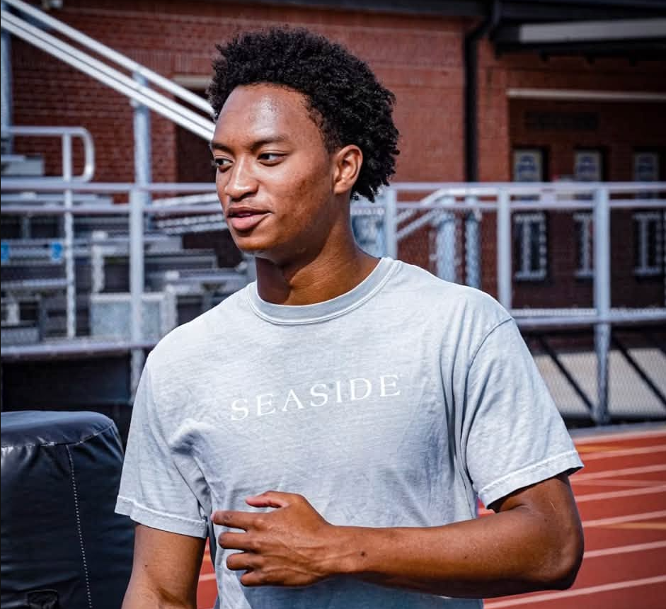 A young man wearing a gray "Seaside" t-shirt stands in front of a brick building.