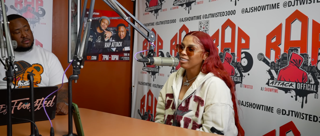 Two people, a man and a woman, sitting at a radio studio desk with a "Rap Attack" poster and other branding visible behind them.