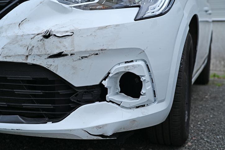 Damaged front bumper of a white car after a traffic accident, close-up view with scratches.
