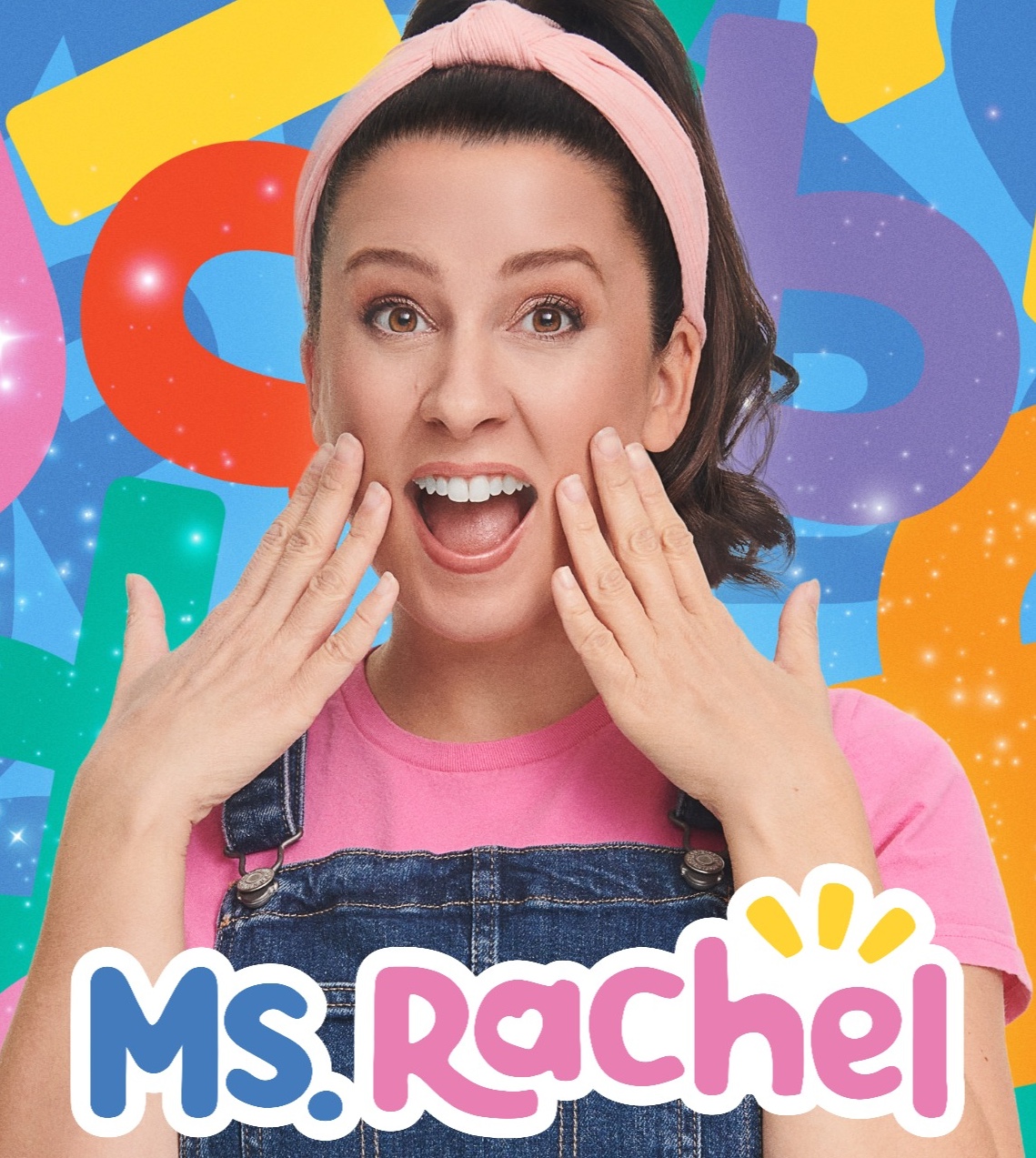 A woman with dark hair wearing a pink headband and denim overalls excitedly gestures with her hands against a colorful abstract background with the text "Ms. Rachel".
